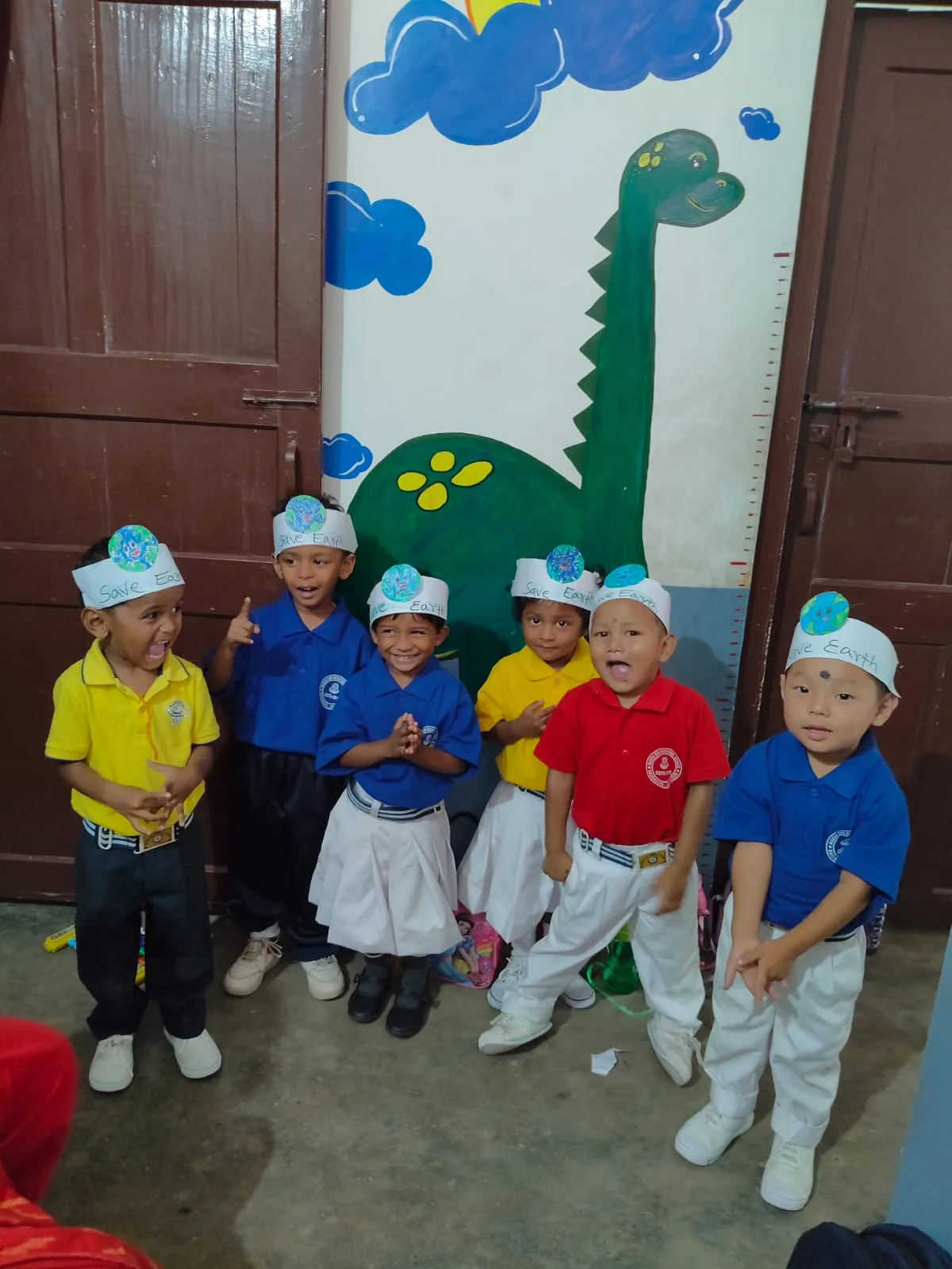 Young MGM School children wearing Save Earth headbands beside a hand-painted dinosaur