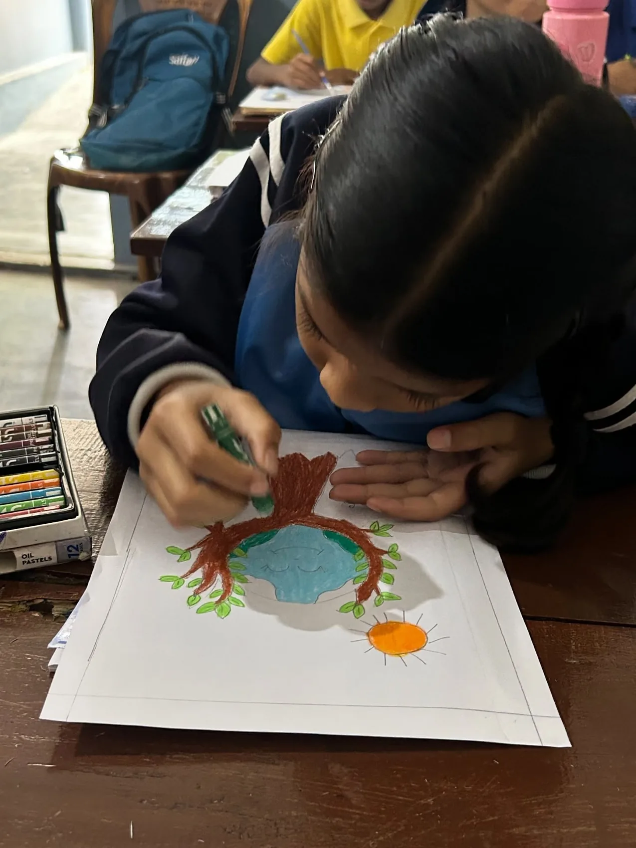 A student drawing a tree and the Earth with pastels